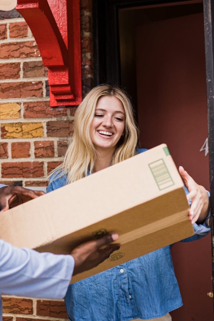 A cheerful woman receives a package from a courier at her door, showcasing friendly delivery service.