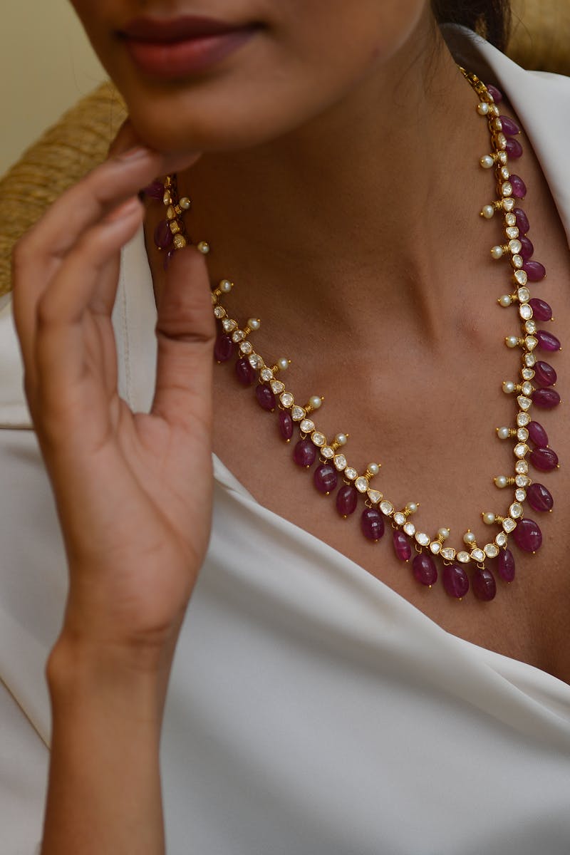 Close-up of a woman showcasing a luxurious ruby and pearl necklace.