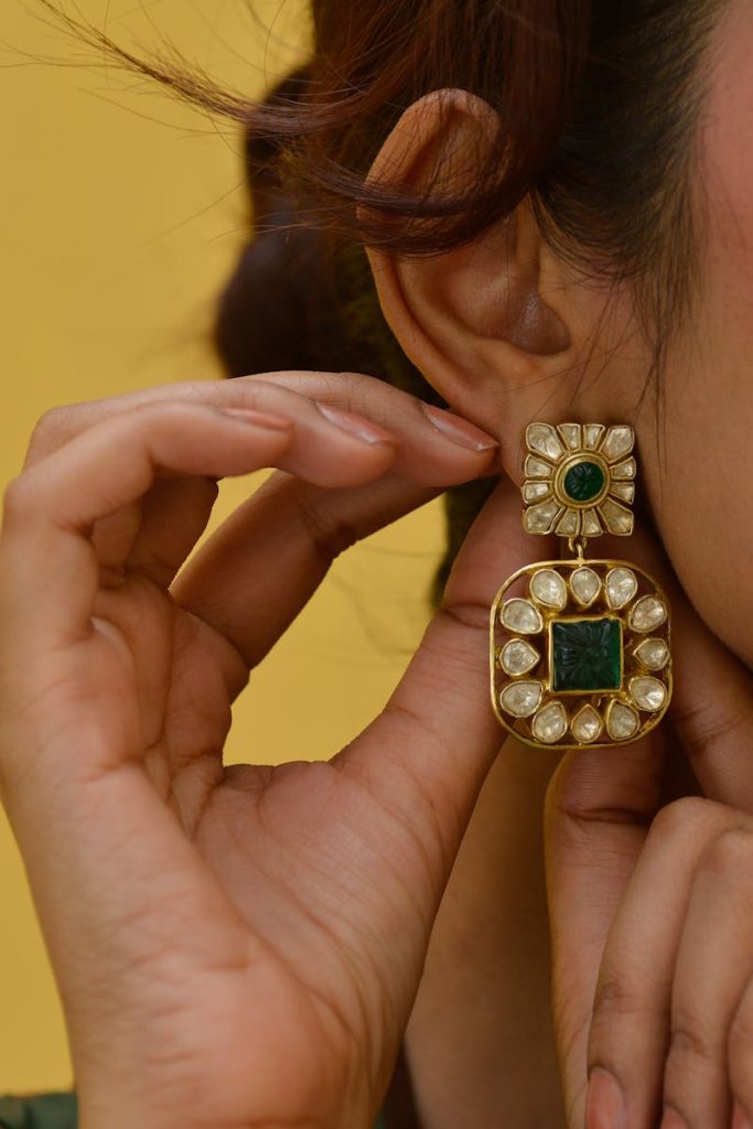 Close-up of emerald and diamond earrings on a woman's ear.